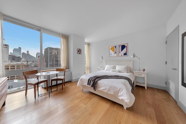 bedroom featuring baseboards, expansive windows, wood finished floors, and a city view