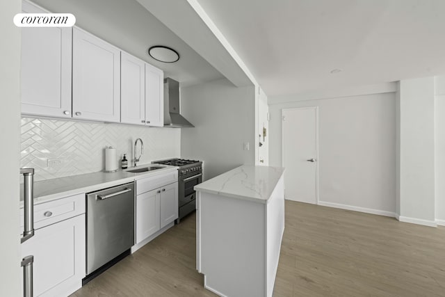 kitchen with appliances with stainless steel finishes, a sink, light wood-type flooring, wall chimney range hood, and backsplash