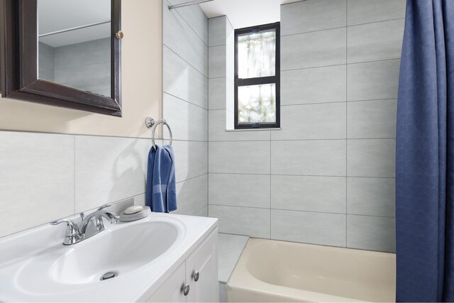 full bath with vanity, backsplash, shower / bath combo with shower curtain, and tile walls