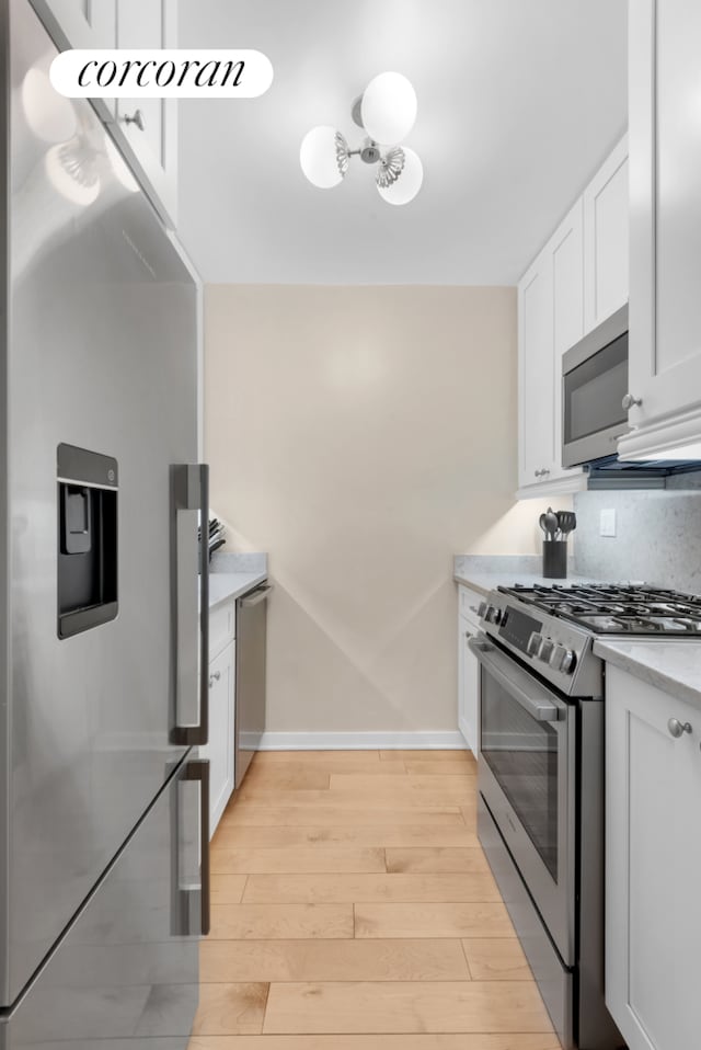 kitchen featuring light wood finished floors, baseboards, decorative backsplash, appliances with stainless steel finishes, and white cabinetry