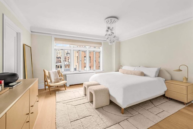 bedroom featuring ornamental molding, light wood-type flooring, and an inviting chandelier