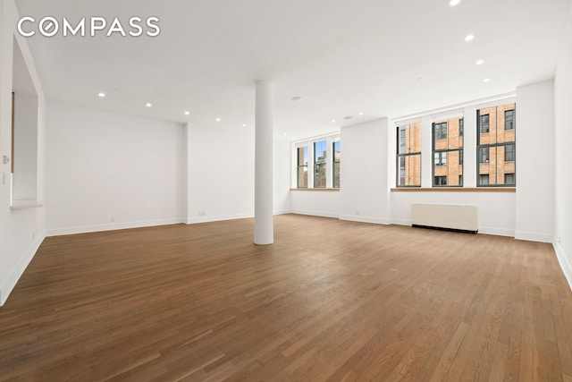 unfurnished living room featuring baseboards, radiator heating unit, wood finished floors, and recessed lighting