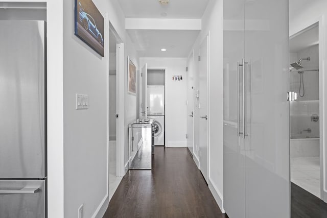 hallway featuring dark wood-style flooring, stacked washer and clothes dryer, and baseboards