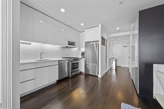 kitchen with dark wood finished floors, stainless steel appliances, white cabinetry, a sink, and modern cabinets