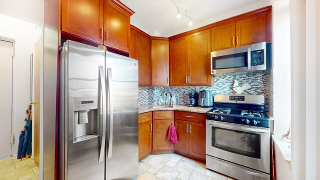 kitchen with tasteful backsplash, stone finish floor, appliances with stainless steel finishes, light stone counters, and a sink