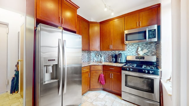 kitchen featuring stone finish flooring, a sink, light stone countertops, stainless steel appliances, and decorative backsplash