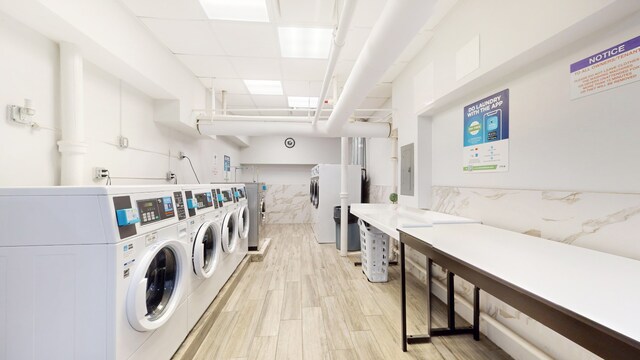 common laundry area featuring tile walls, washer and clothes dryer, light wood finished floors, wainscoting, and electric panel