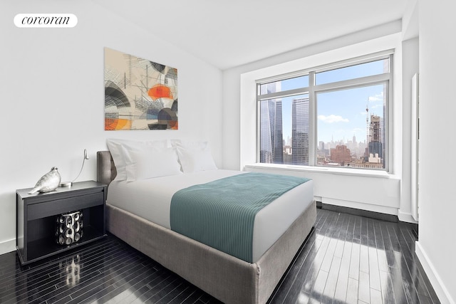bedroom with dark wood-style floors, baseboards, and a skyline view