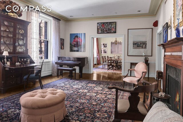 sitting room featuring baseboards, a premium fireplace, wood finished floors, an inviting chandelier, and crown molding