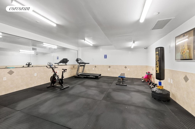 workout room featuring a wainscoted wall, visible vents, and tile walls