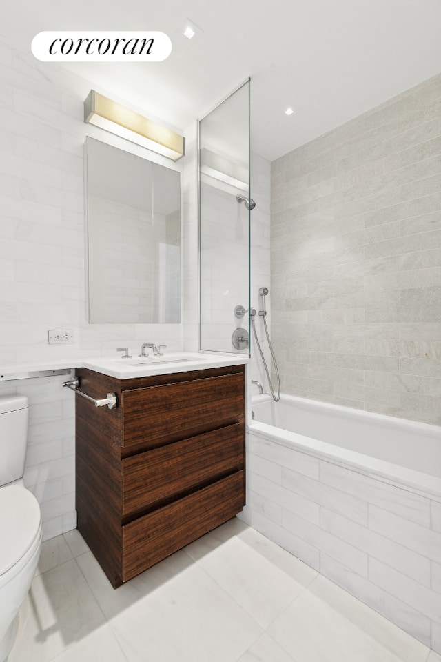 bathroom featuring toilet, tiled shower / bath combo, tile patterned flooring, vanity, and tile walls