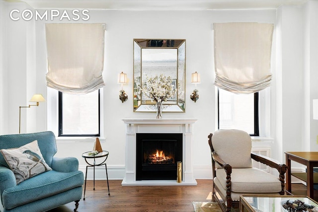 living area with a warm lit fireplace, wood finished floors, visible vents, and baseboards