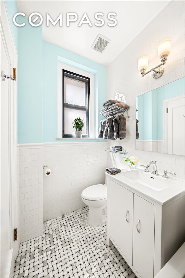 bathroom featuring visible vents, wainscoting, toilet, vanity, and tile walls