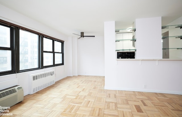 empty room with a wall unit AC, radiator heating unit, baseboards, and ceiling fan