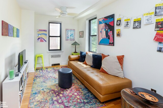 living room with light wood-type flooring, baseboards, ceiling fan, and radiator heating unit