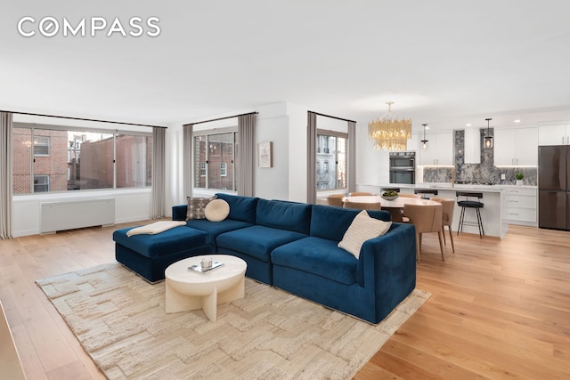 living room featuring light wood-style flooring, radiator, and an inviting chandelier