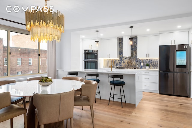 kitchen with light wood-style flooring, a kitchen island with sink, stainless steel appliances, light countertops, and backsplash