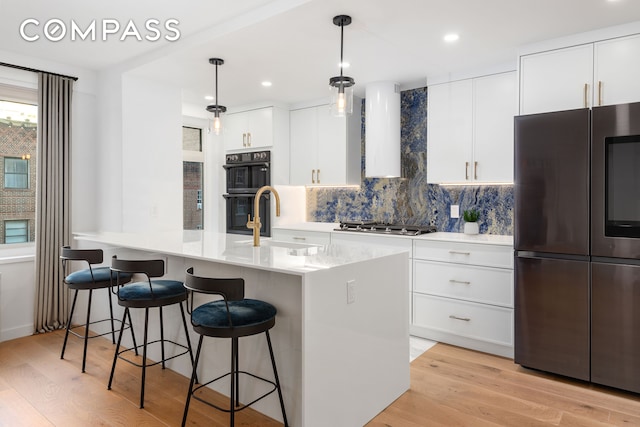 kitchen featuring a breakfast bar area, light wood-type flooring, range hood, appliances with stainless steel finishes, and a sink