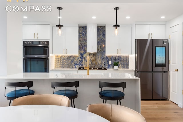 kitchen featuring pendant lighting, a breakfast bar area, light wood-type flooring, white cabinets, and stainless steel appliances