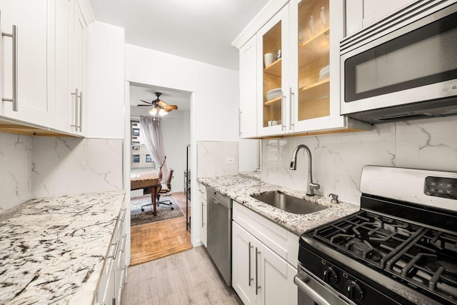 kitchen with stainless steel appliances, glass insert cabinets, white cabinets, a sink, and light stone countertops