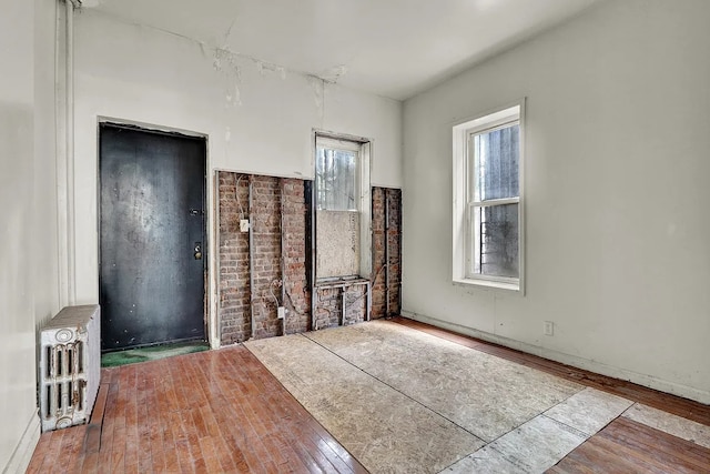 unfurnished room with baseboards, heating unit, a wealth of natural light, and hardwood / wood-style flooring