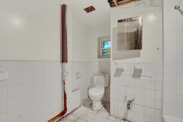 bathroom with toilet, tile patterned floors, tile walls, and a wainscoted wall
