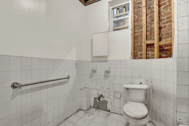 half bath with marble finish floor, a wainscoted wall, toilet, and tile walls