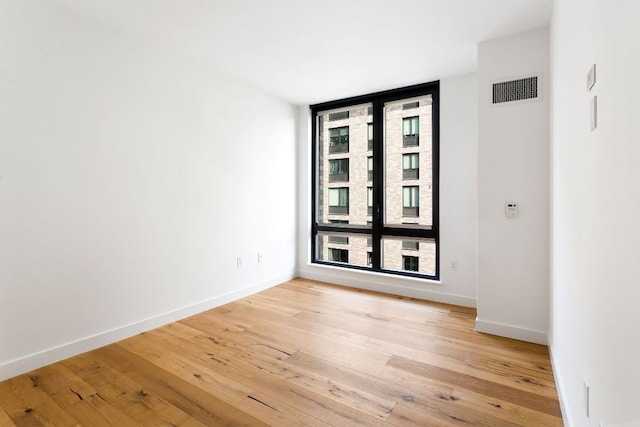 unfurnished room featuring light wood-style flooring, a wall of windows, visible vents, and baseboards