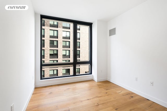 empty room featuring baseboards, light wood-type flooring, visible vents, and floor to ceiling windows