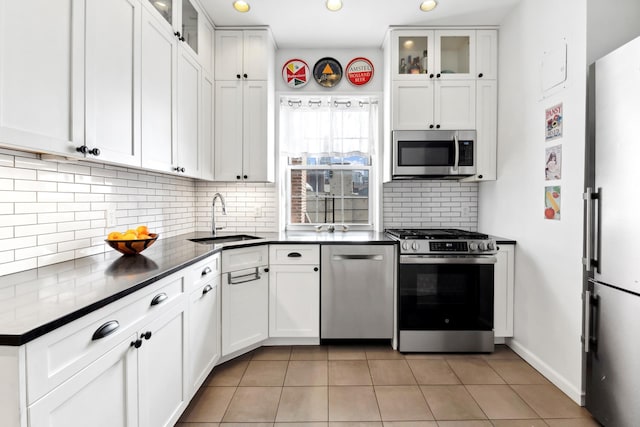 kitchen with stainless steel appliances, dark countertops, decorative backsplash, white cabinets, and a sink