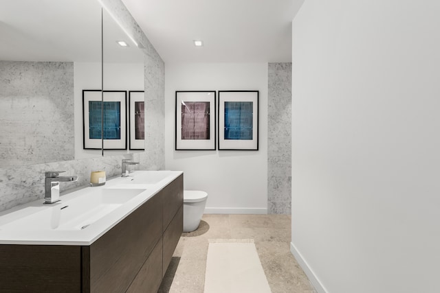 bathroom featuring double vanity, baseboards, toilet, and a sink