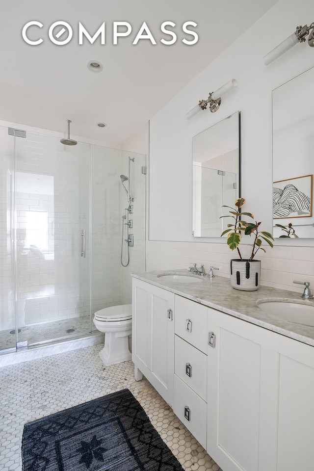 full bath featuring double vanity, a sink, toilet, and a shower stall