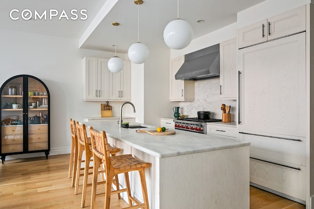 kitchen with a breakfast bar area, stove, a sink, light countertops, and wall chimney exhaust hood