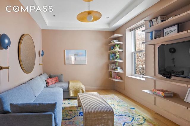 living room with light wood-style floors, baseboards, and a tray ceiling