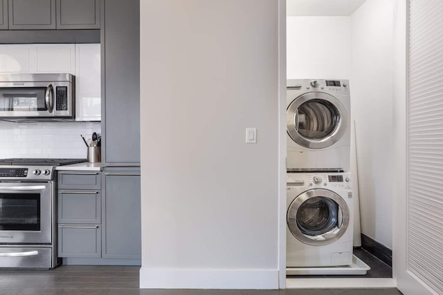 laundry room featuring laundry area, baseboards, stacked washing maching and dryer, and wood finished floors