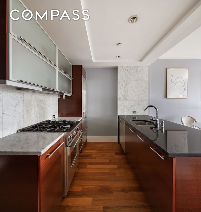 kitchen featuring a sink, stainless steel range, dark stone countertops, dark wood finished floors, and glass insert cabinets