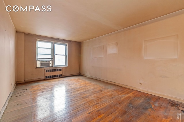 empty room featuring cooling unit, radiator heating unit, baseboards, and hardwood / wood-style flooring