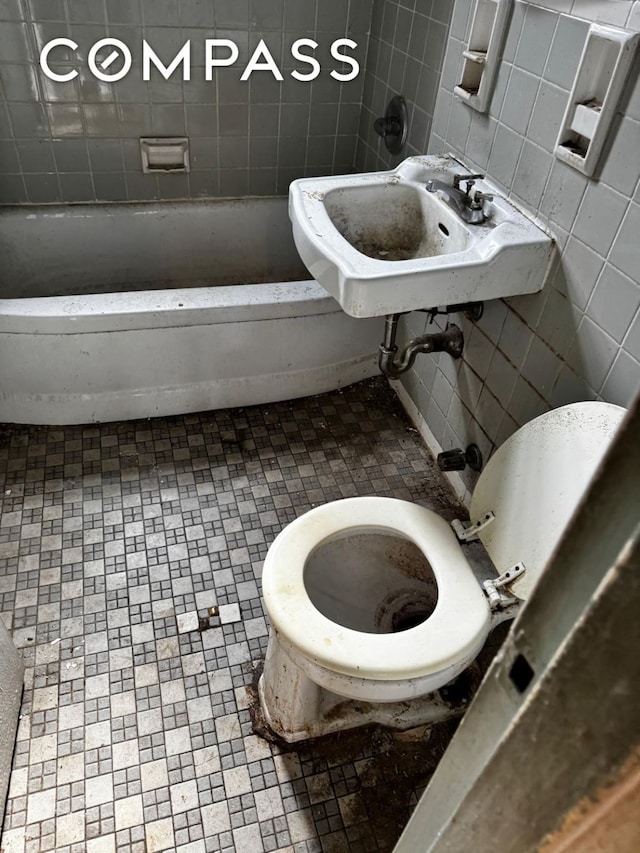 bathroom featuring toilet, a bathing tub, tile walls, and a sink