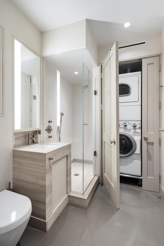 bathroom with a stall shower, toilet, stacked washer / drying machine, tile patterned flooring, and vanity