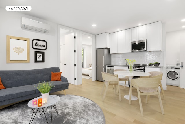 kitchen featuring visible vents, washer / clothes dryer, stainless steel appliances, an AC wall unit, and white cabinetry