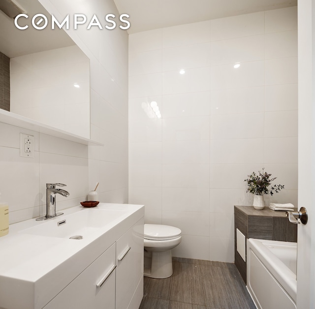 bathroom featuring tile walls, toilet, vanity, and a tub