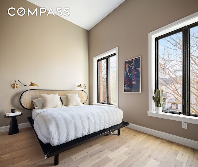 bedroom featuring light wood finished floors, baseboards, and vaulted ceiling