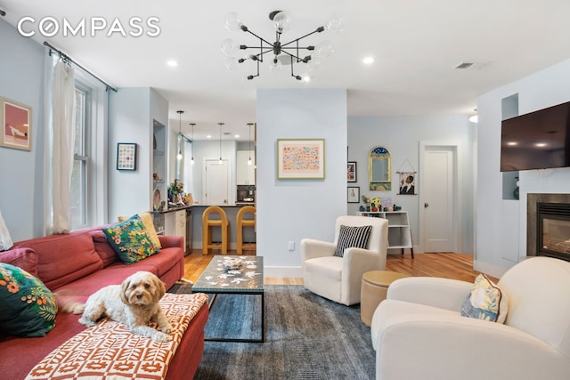 living room featuring wood finished floors, a chandelier, recessed lighting, a glass covered fireplace, and baseboards