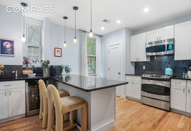 kitchen featuring dark countertops, appliances with stainless steel finishes, beverage cooler, and light wood finished floors