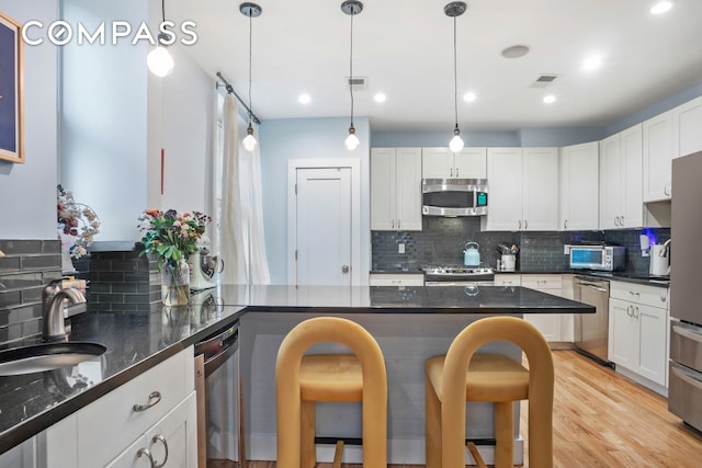 kitchen with appliances with stainless steel finishes, a sink, a breakfast bar area, tasteful backsplash, and recessed lighting