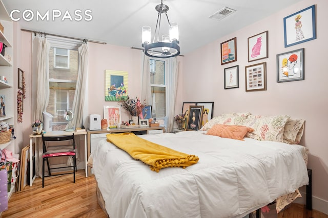 bedroom with light wood-style flooring, visible vents, and an inviting chandelier