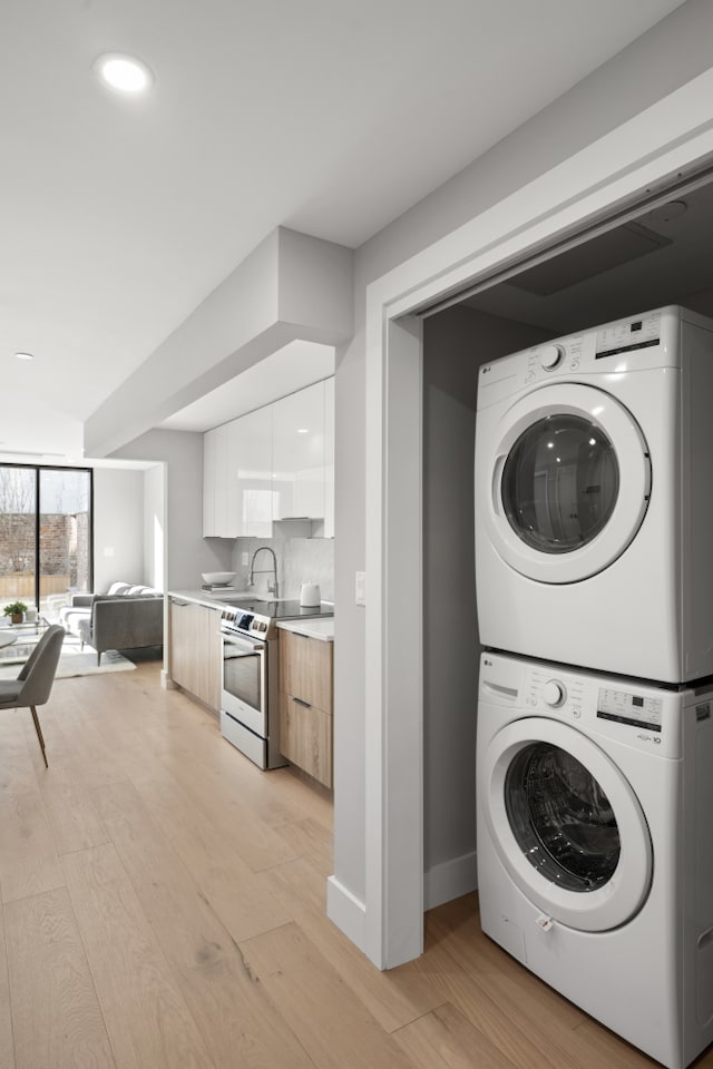 laundry area featuring stacked washer and dryer, laundry area, a sink, baseboards, and light wood finished floors