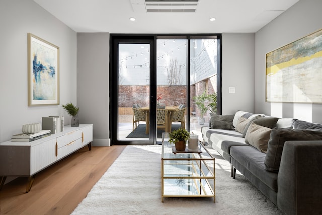 living room featuring light wood finished floors, a wall of windows, visible vents, and recessed lighting