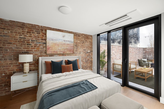 bedroom with expansive windows, brick wall, light wood-style floors, and access to exterior