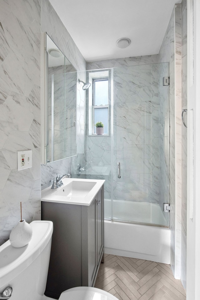 bathroom featuring toilet, bath / shower combo with glass door, tile walls, and vanity